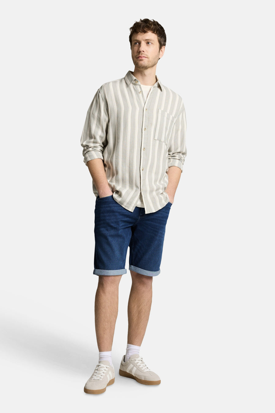 Jeansshort van donkerblauw denim van TOM TAILOR, met omgeslagen pijpen en gedragen met een gestreept overhemd en witte sneakers.
