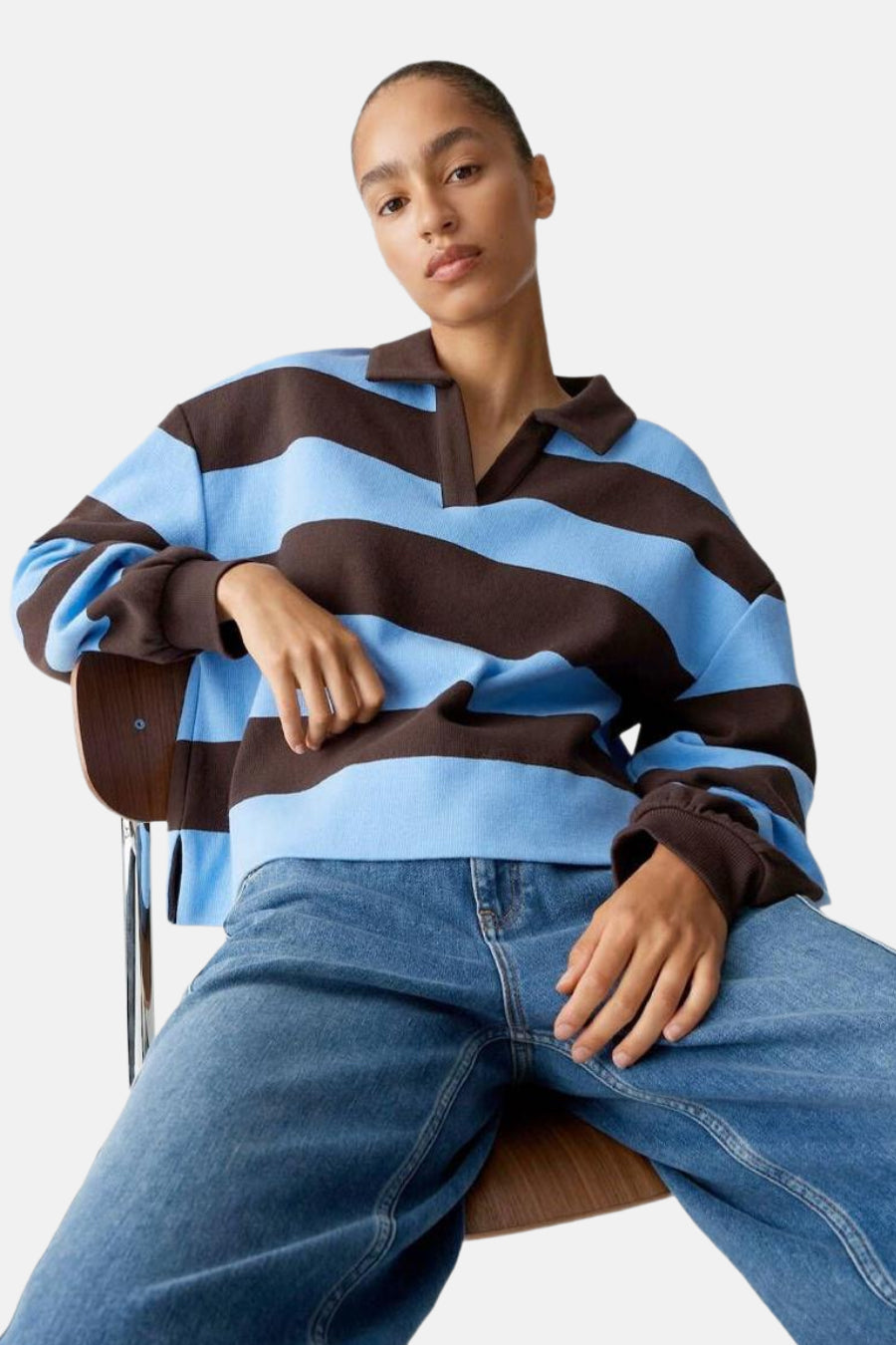 Vrouw in blauw en bruin gestreepte trui en jeans.
