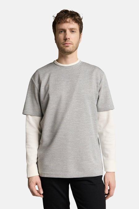 Grijs T-shirt van TOM TAILOR, met korte mouwen en een subtiel gestreept patroon, gedragen over een crèmekleurig shirt met lange mouwen.
