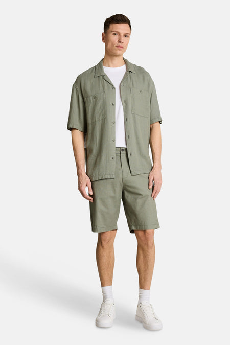 Groene short van TOM TAILOR, gecombineerd met een groen overhemd en wit T-shirt, witte sokken en sneakers.
