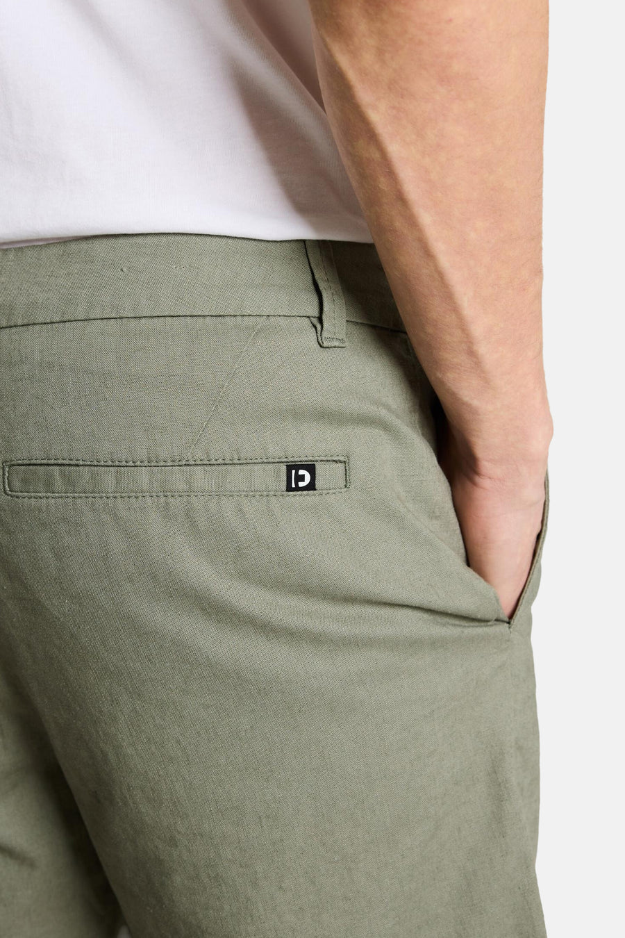Groene short van TOM TAILOR, met achterzak en logo, en steekzak waarin een hand zit.
