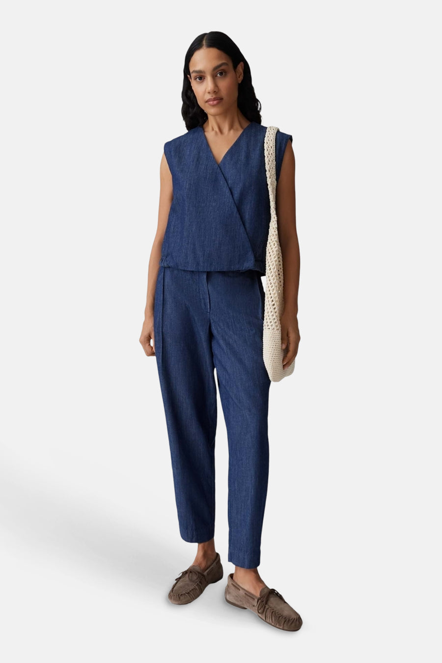 Donkerblauwe mouwloze denim blouse van OPUS met overslag-V-hals, gecombineerd met bijpassende broek, bruine mocassins en een crèmekleurige gehaakte tas.