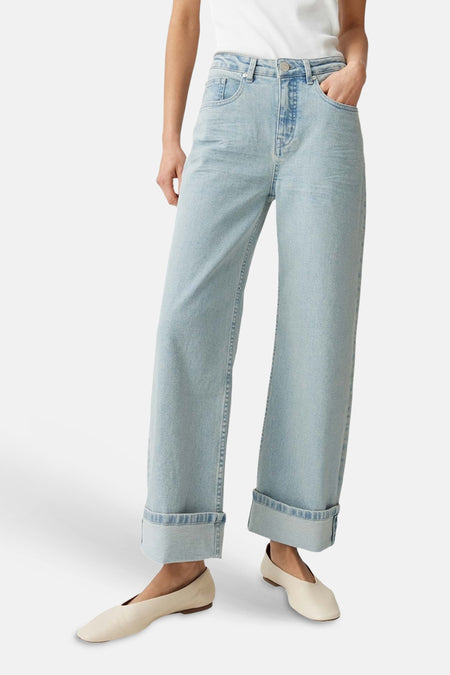 Jean large bleu clair OPUS avec ourlets retroussés, porté avec un haut blanc et des chaussures claires, vue de dos.