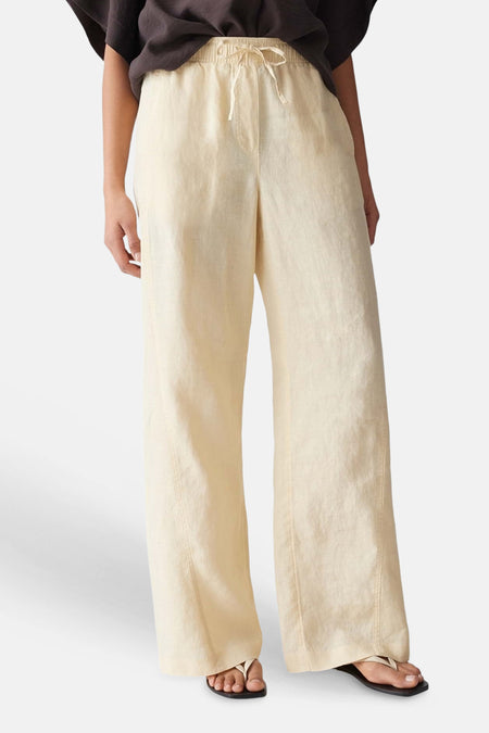 Lichtgele, wijde damesbroek met elastische tailleband van OPUS, met trekkoord en verticale naden, gestyled met donker shirt en sandalen.