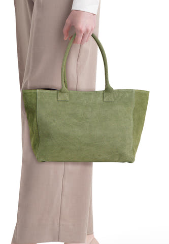 Khakigroene suède shoppertas van Access® met twee handvatten, vastgehouden door een persoon in een beige broek.