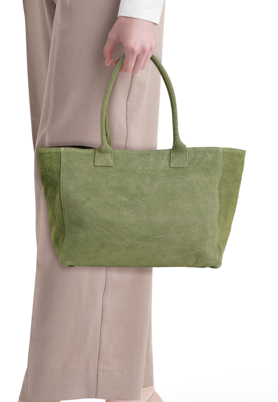 Khakigroene suède shoppertas van Access® met twee handvatten, vastgehouden door een persoon in een beige broek.