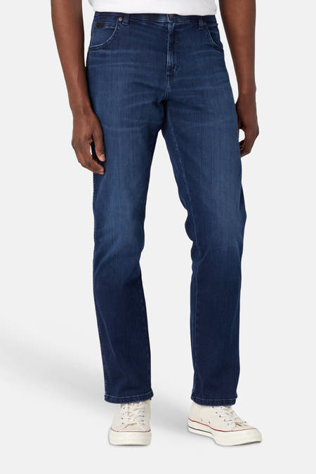 Donkerblauwe straight jeans van Wrangler met lichte wassing, staand gedragen met witte sneakers.