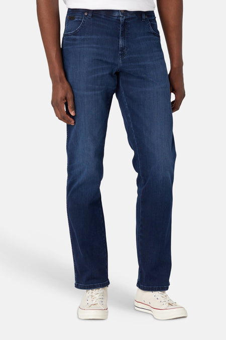 Donkerblauwe straight jeans van Wrangler met lichte wassing, staand gedragen met witte sneakers.