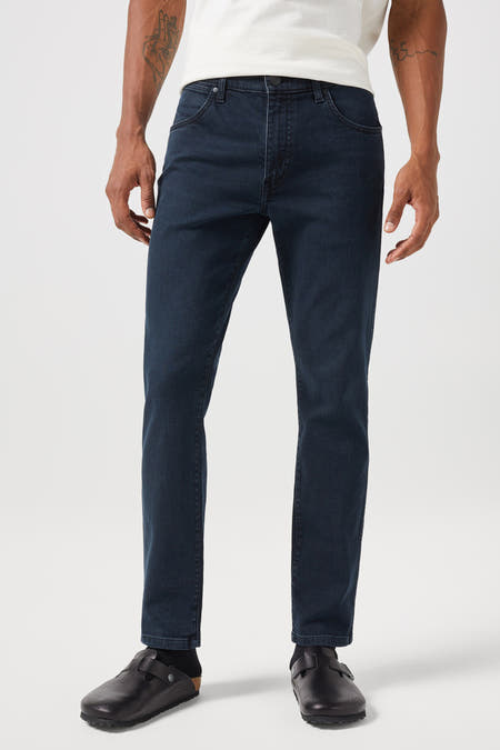 Donkerblauwe tapered jeans van Wrangler, met een subtiele textuur en styling met een t-shirt en leren muiltjes.
