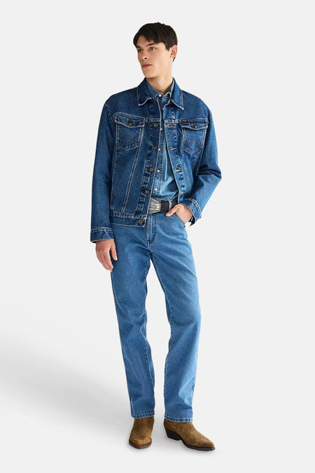 Middelblauwe rechte jeans van denim van Wrangler, gedragen door een man met een denim jack en bruine laarzen.