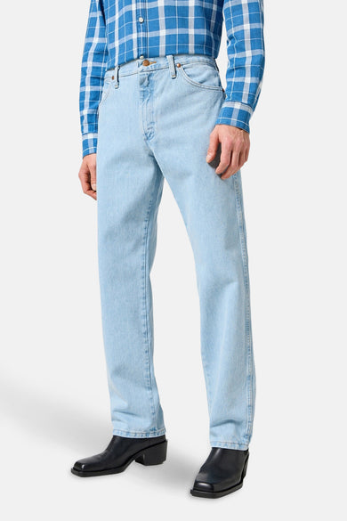 Jeans straight van lichtblauw denim van Wrangler, gecombineerd met een blauw geruit overhemd en zwarte laarzen.