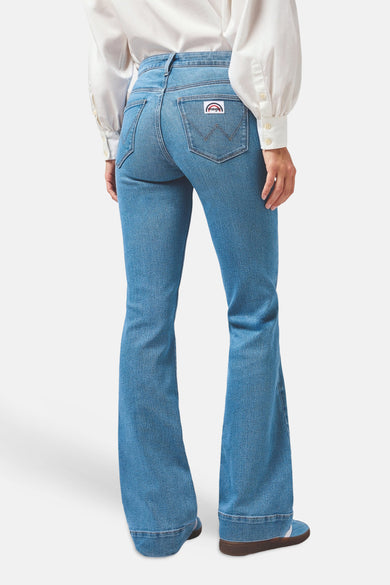 Lichte blauwe denim flared jeans van Wrangler® met het logo op de rechter achterzak, gedragen met een wit overhemd en sneakers.
