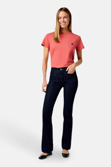 Jeans flared donkerblauw denim van Wrangler®, gecombineerd met een koraalkleurig T-shirt en zwarte platte schoenen.
