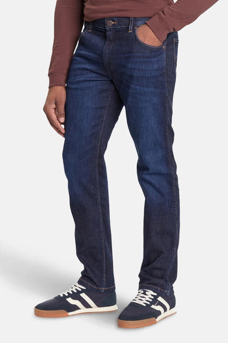 Jeans straight donkerblauw denim van Wrangler®, getoond in zijaanzicht, gecombineerd met bruin shirt en blauwe sneakers.

