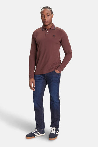 Rechte jeans van donkerblauw denim van Wrangler®, gestyled met bruine polo met lange mouwen en donkerblauwe schoenen.