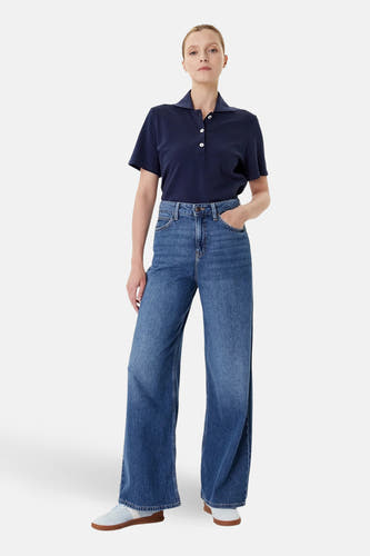 Blauw denim Stella jeans wide van Lee®, gedragen met een donkerblauw poloshirt en blauwe schoenen.