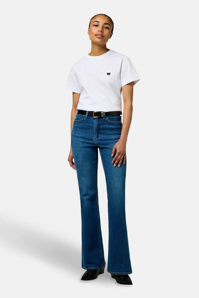 Uitlopende jeans van blauw denim van Wrangler, met zwarte riem en wit T-shirt met logo.
