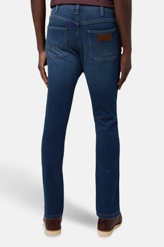 Boutons de fermeture éclair sur des jeans Wrangler en denim bleu foncé, avec un logo marron sur la poche arrière.