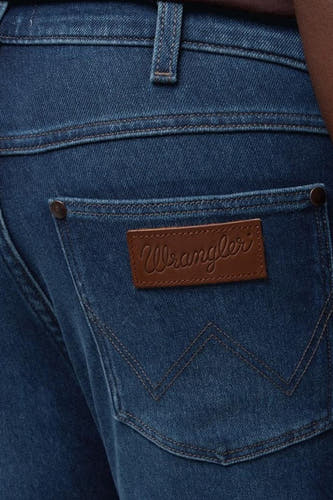 Jean tapered bleu marine en denim de Wrangler, avec des boutons caractéristiques sur la poche arrière et un étiquette en cuir.
