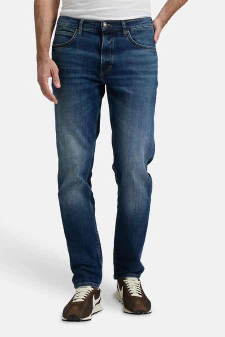 Jean tapered bleu foncé de Lee®, vue arrière d'un homme avec un t-shirt blanc et des baskets.