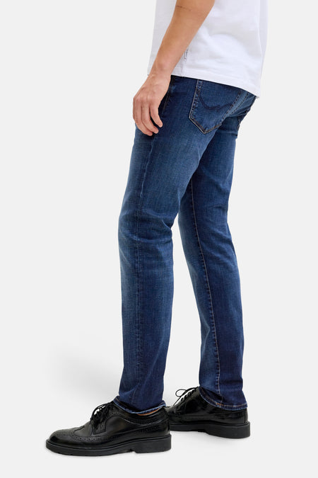 Slim fit jeans mid blue denim van JACK & JONES JEANS INTELLIGENCE, met zwarte brogues en een wit T-shirt, zijaanzicht.
