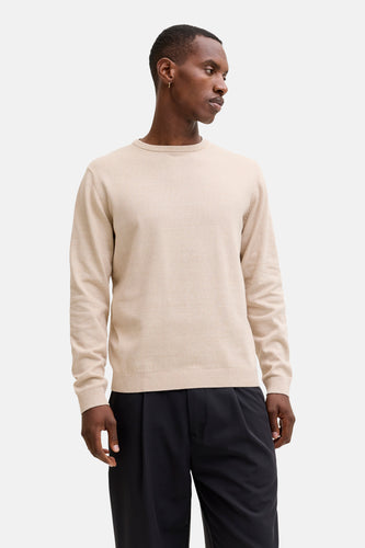 Man met beige trui en zwarte broek.