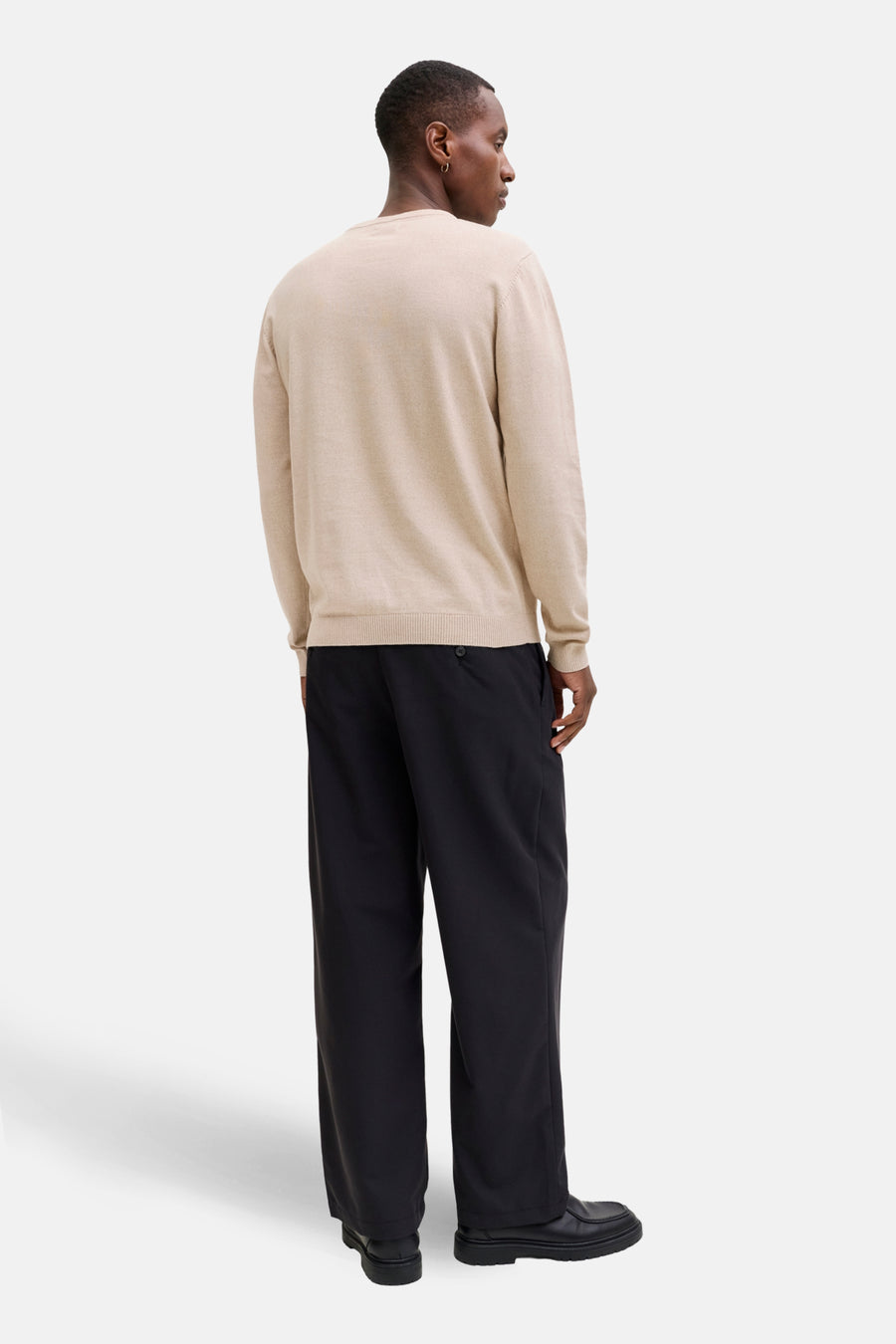 Man van achteren in beige trui en zwarte broek.
