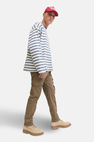 Bruine cargobroek van JACK & JONES JEANS INTELLIGENCE, gecombineerd met een gestreepte trui, rode pet en beige veterschoenen.
