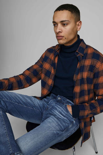 Slim fit jeans mid blue denim van JACK & JONES JEANS INTELLIGENCE, gedragen met een donkerblauwe coltrui en een bruin en donkerblauw geruit overhemd.

