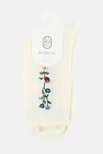 Crèmekleurige sokken van BIRDLAND met geborduurde bloemen, geribbelde textuur en ruches, aan een labelhanger.