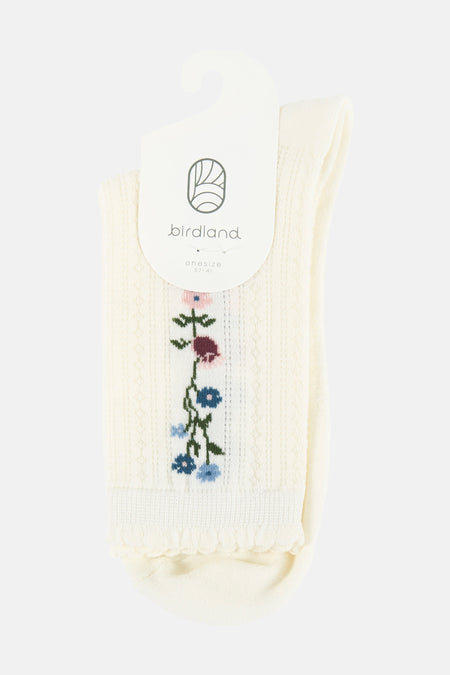 Crèmekleurige sokken van BIRDLAND met geborduurde bloemen, geribbelde textuur en ruches, aan een labelhanger.