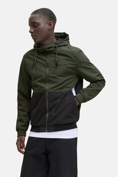Groene regenjas van ORIGINALS BY JACK & JONES, met zwarte kleurblokken en capuchon, gedragen over een wit T-shirt en zwarte broek.
