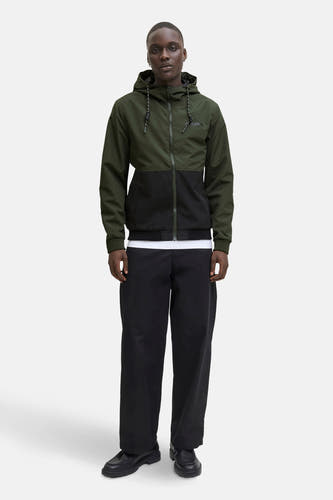 Groene regenjas van ORIGINALS BY JACK & JONES, met een zwarte blokkleur, capuchon met trekkoord, en gedragen over een wit T-shirt en zwarte broek.
