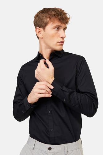 Zwart overhemd met lange mouwen van PREMIUM by JACK & JONES, detailopname van een man die de mouw dichtknoopt, met grijze broek.