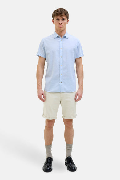 Ecru short van JACK & JONES JEANS INTELLIGENCE, gecombineerd met een lichtblauw overhemd, sokken en nette schoenen.
