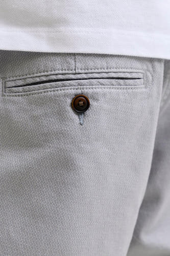 Grijze short van JACK & JONES JEANS INTELLIGENCE met subtiel geweven patroon, een paspelzak met donkerbruine knoop en een wit poloshirt.