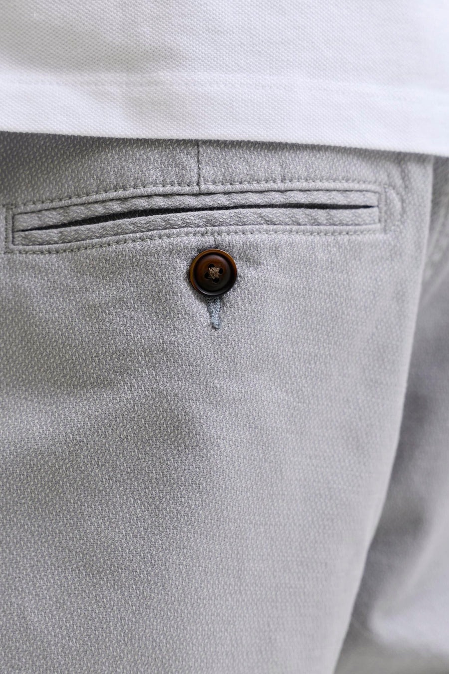 Grijze short van JACK & JONES JEANS INTELLIGENCE met subtiel geweven patroon, een paspelzak met donkerbruine knoop en een wit poloshirt.