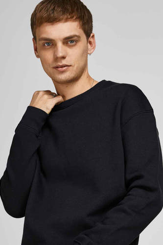 Zwarte sweater van CORE BY JACK & JONES, met ronde hals en lange mouwen, gedragen door een man met ringen.
