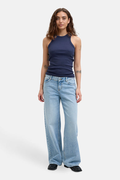 Blauwe mouwloze top van JJXX, gedragen met een lichtblauwe wijde jeans en zwarte schoenen.