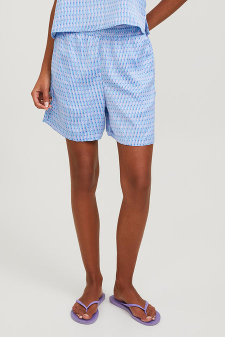Blauwe short van JJXX met verticaal streepjespatroon gedragen met paarse slippers.
