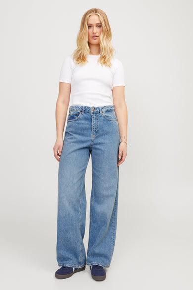 Wijde jeans van denim in middenblauw van JJXX, met een model in een wit shirt en blauwe schoenen.