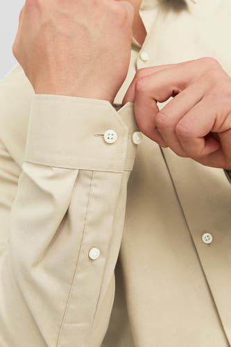 Beige heren overhemd met lange mouwen van PREMIUM by JACK & JONES, close-up van een man die de knoop van de manchet sluit.