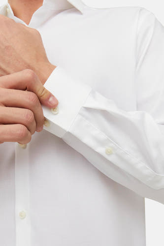 Chemise blanche à manches longues de PREMIUM by JACK & JONES, avec un homme qui ferme le bouton.