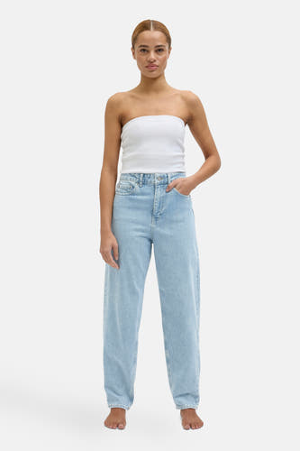 Lichtblauwe mom jeans van JJXX, gedragen met een witte top, met een hand in de zak.
