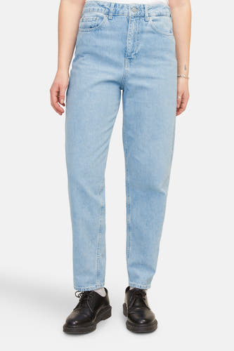 Lichtblauwe mom jeans van JJXX, gecombineerd met zwarte schoenen en witte sokken tegen een effen achtergrond.
