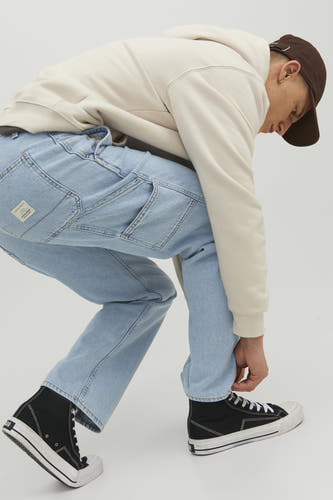 Un homme en un hoodie beige, un short de denim bleu et des baskets noires hautes.