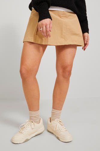 Beige korte rok van JJXX, met een A-lijn silhouet, gecombineerd met crèmekleurige sneakers en sokken.
