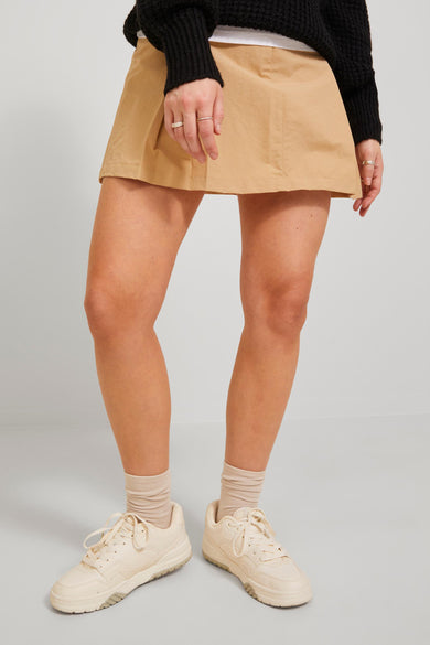 Jupe courte beige de JJXX, avec une silhouette en A, associée à des sneakers crème et des chaussettes.