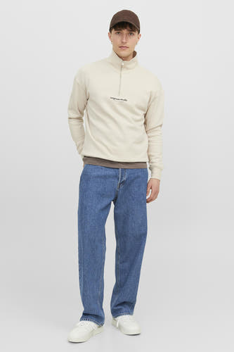 Wijd uitlopende jeans van blauw denim van JACK & JONES JEANS INTELLIGENCE, gecombineerd met een beige trui en bruine pet.
