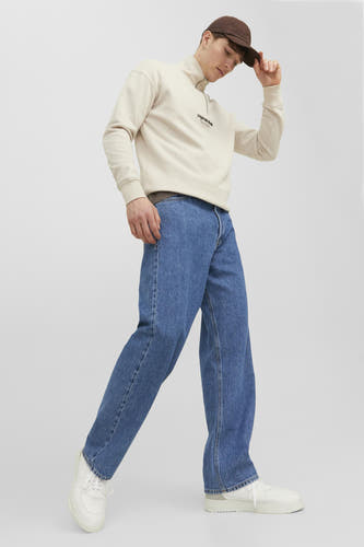 Jean en denim bleu large de JACK & JONES JEANS INTELLIGENCE, porté avec un sweat-shirt beige et des baskets blanches, avec une casquette marron.